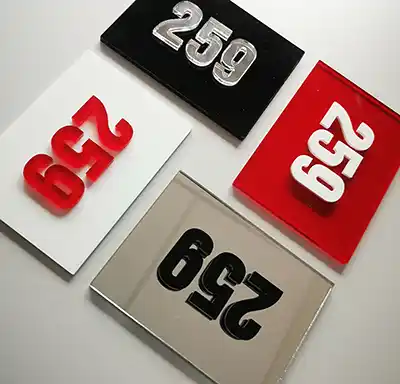 Quatre plaques rectangulaires, chacune affichant le nombre 259 dans des couleurs et des finitions différentes : noir avec chiffres argentés, rouge avec chiffres blancs, blanc avec chiffres rouges, et une surface miroir avec chiffres noirs.