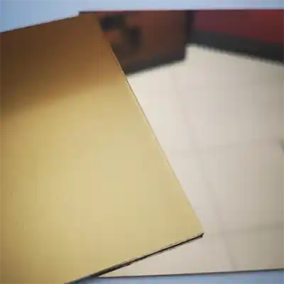 Une feuille rectangulaire d'acrylique miroir de couleur or est placée sur une surface réfléchissante, montrant un reflet partiel d'un sol carrelé et d'un mur à l'arrière-plan.