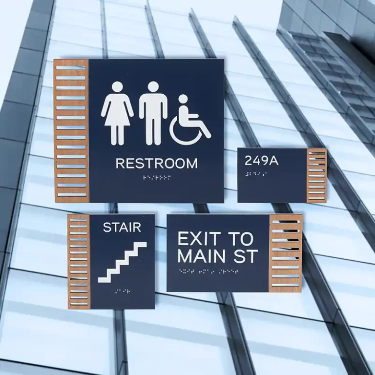 Panneaux avec éléments tactiles, dont un panneau de toilettes avec des symboles dhomme, de femme et de fauteuil roulant, un panneau descalier, un panneau « Sortie vers Main St » et un numéro de chambre « 249A ». Le fond est une façade de bâtiment en verre moderne.