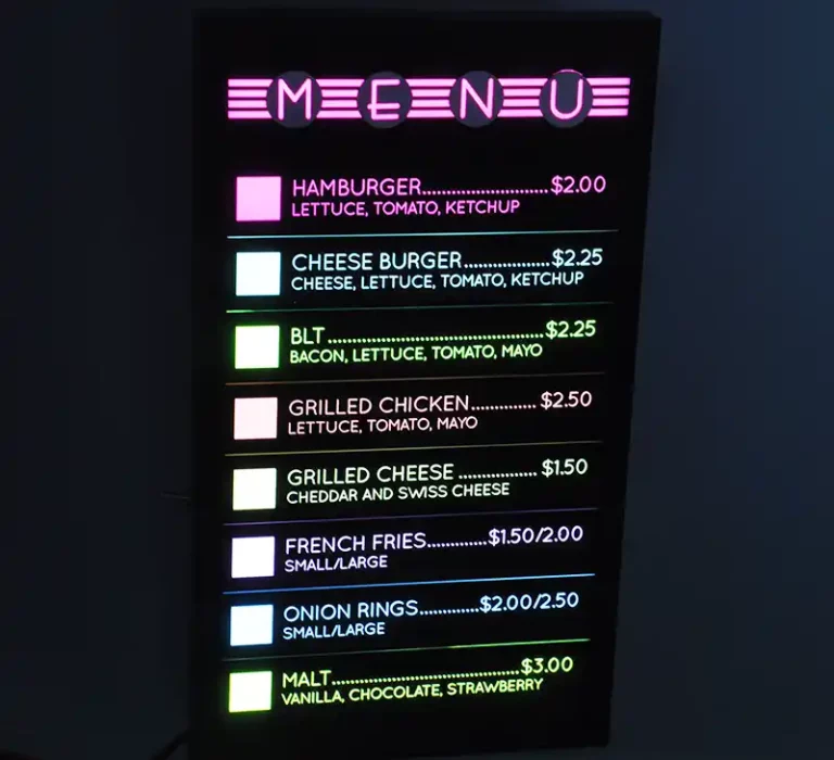 Menu illuminé avec options : hamburger 2 $, cheeseburger 2,25 $, BLT 2,50 $, poulet grillé 2,50 $, sandwich au fromage grillé 1,50 $, frites 1,50 $/2 $, rondelles doignon 2 $/2,50 $, malt 3 $. Les garnitures comprennent de la laitue, des tomates, du ketchup, du bacon, de la mayonnaise et du fromage.