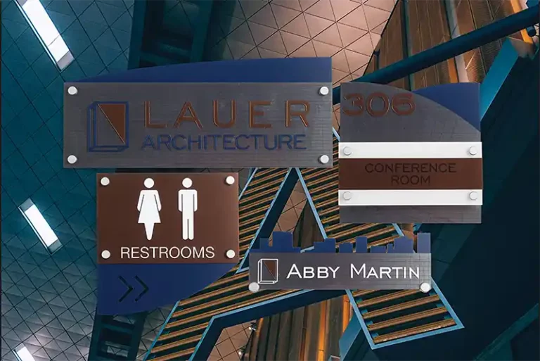 Un groupe de panneaux intérieurs comprenant « Lauer Architecture », « Toilettes » avec des icônes masculines et féminines, « Salle de conférence », « 306 » et « Abby Martin ». Éléments de design moderne aux couleurs bleues et marron. Plafond avec carreaux à motifs en arrière-plan.