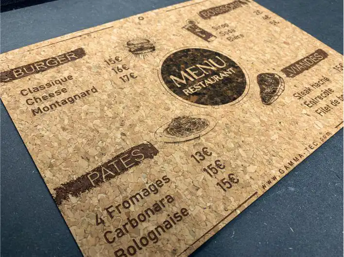 Un menu de restaurant en liège avec des sections pour les hamburgers, les pâtes, le poisson et les viandes. Les prix des plats comme le cheese burger, la carbonara et le steak sont indiqués. Le menu est texturé et marqué « www.gamma-tec.com » dans le coin.