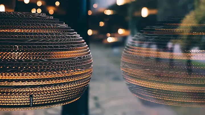 Gros plan dune suspension sphérique texturée de Think Paper avec un éclairage chaleureux, se reflétant sur une fenêtre floue. Larrière-plan présente un doux effet bokeh de lumières supplémentaires, créant une ambiance chaleureuse.