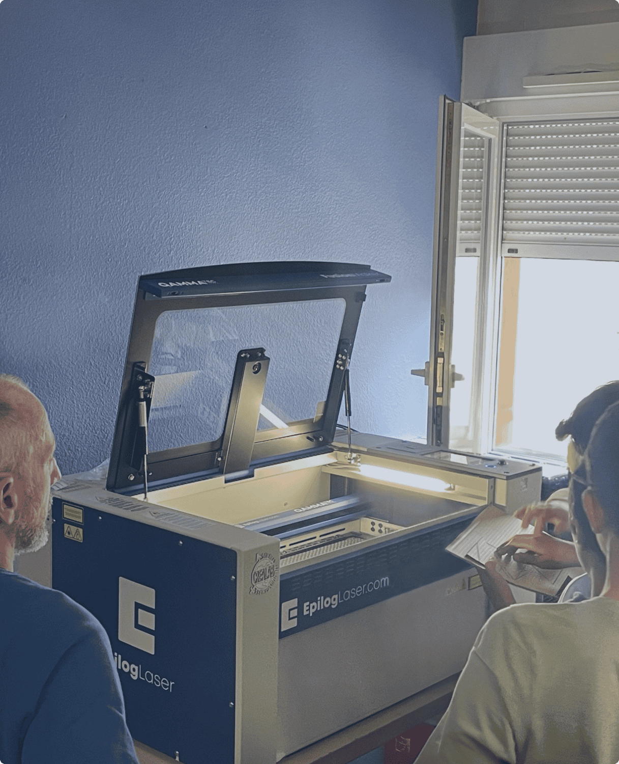 Des enfants observent une démonstration pédagogique autour d'une machine laser Epilog dans une pièce lumineuse.