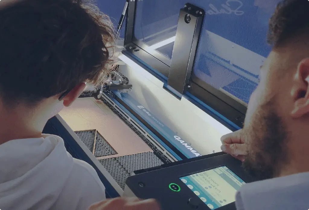 Deux personnes observent de près une machine de découpe laser en fonctionnement, l'une interagissant avec le panneau de commande numérique et l'autre surveillant la zone de découpe - une démonstration de l'enseignement pratique de la découpe laser.