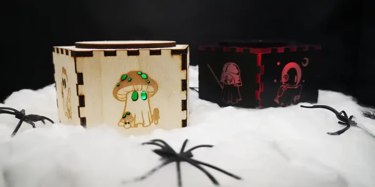 Une boîte en bois et une en acrylique reposent sur un lit de tissu blanc. Les boîtes lumineuses présentent des fantômes découpés ou gravés au laser pour Halloween.