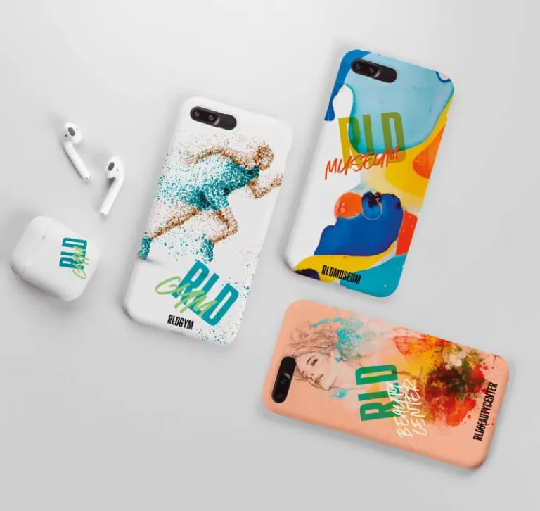 Trois étuis de téléphone illustrés, réalisés avec la technologie de l'imprimante sur objet, et une paire d'écouteurs sans fil dans un étui de chargement blanc sont présentés sur une surface blanche. Les étuis présentent des motifs artistiques et colorés avec "BLD" et d'autres mots.