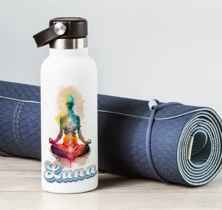 Une bouteille d'eau blanche étiquetée "Luna" présente une illustration colorée d'une figure méditante avec des symboles de chakra, réalisée à l'aide d'une imprimante sur objet. Elle est posée à côté d'un tapis de yoga bleu roulé sur une surface en bois clair.