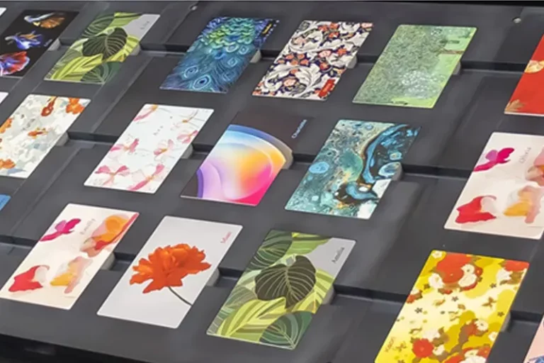 Un présentoir contient plusieurs cartes rectangulaires disposées en rangées, chacune présentant un motif coloré différent, y compris des motifs floraux, de l'art abstrait et des illustrations inspirées de la nature créées avec la technologie de l'imprimante sur objet.