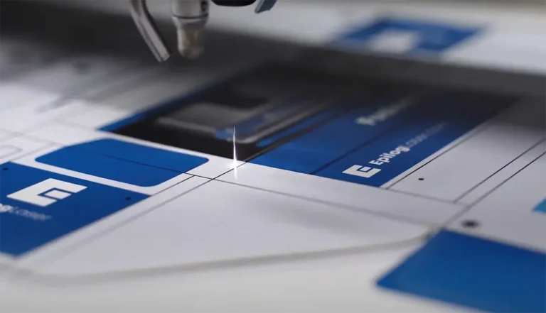 Un découpeur laser co2 découpe avec précision une feuille de matériau imprimé avec des graphiques bleus et blancs, en suivant des lignes marquées sur la surface.