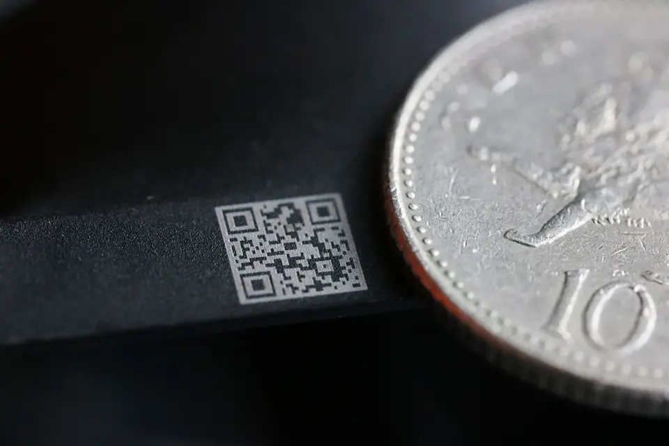 Une image en gros plan montrant un petit code QR imprimé à côté de la tranche d'une pièce de monnaie, mettant en évidence la précision du marquage industriel dans la production de codes minuscules pour l'identification des produits.