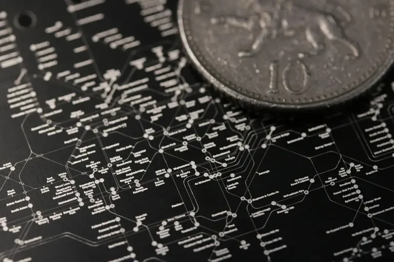 Gros plan d'un diagramme détaillé, blanc sur noir, avec des lignes et des étiquettes interconnectées, ressemblant à une carte de transport ou de réseau, partiellement couvert par une pièce d'argent marquée du chiffre 10 et du marquage industriel.