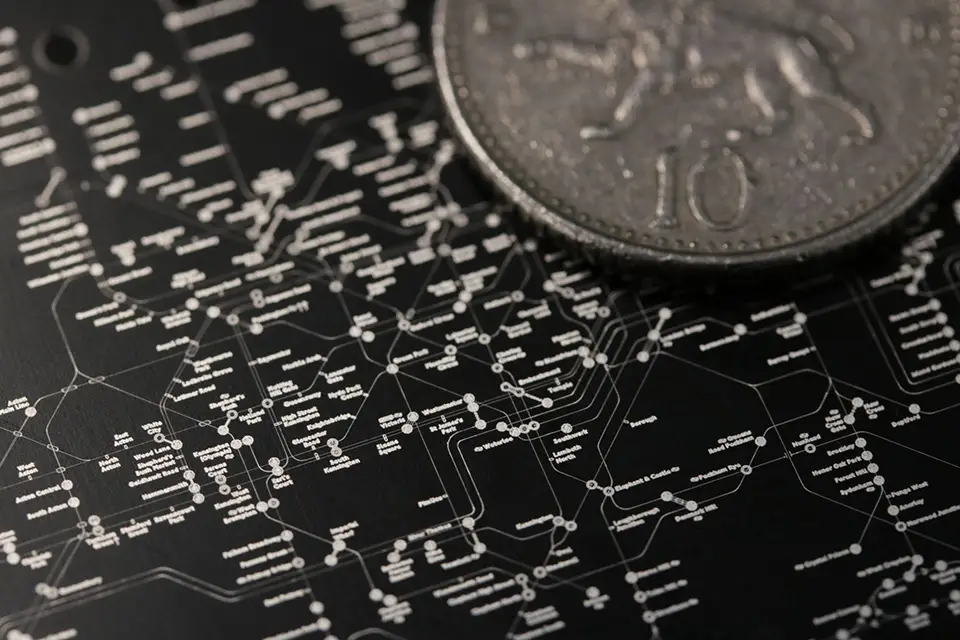 Gros plan d'un diagramme détaillé, blanc sur noir, avec des lignes et des étiquettes interconnectées, ressemblant à une carte de transport ou de réseau, partiellement couvert par une pièce d'argent marquée du chiffre 10 et du marquage industriel.