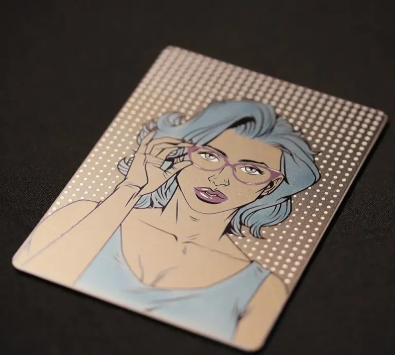 Une carte rectangulaire sur une surface sombre représente une femme aux cheveux bleus, portant des lunettes et un haut de couleur claire, tenant la monture de ses lunettes. L'arrière-plan présente un motif de points blancs ressemblant aux détails complexes d'un marqueur au laser.