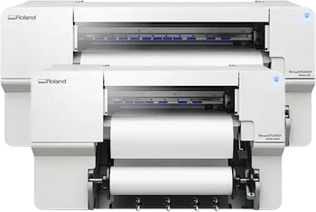 Deux imprimantes blanches Roland VersaSTUDIO imprimante/découpeuse jet d'encre sont placées l'une derrière l'autre, toutes deux chargées de rouleaux de papier vierge. Ces machines modernes affichent des voyants bleus et sont prêtes à effectuer des tâches d'impression et de découpe précises.