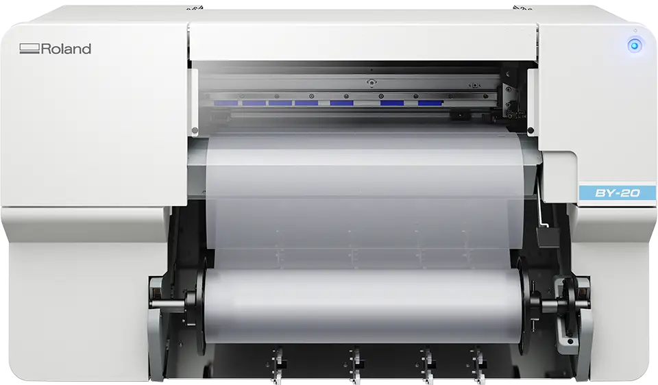 Imprimante Roland BY-20 impression DTF blanche avec un rouleau de matériau transparent partiellement chargé visible par l'ouverture avant, sur un fond uni.