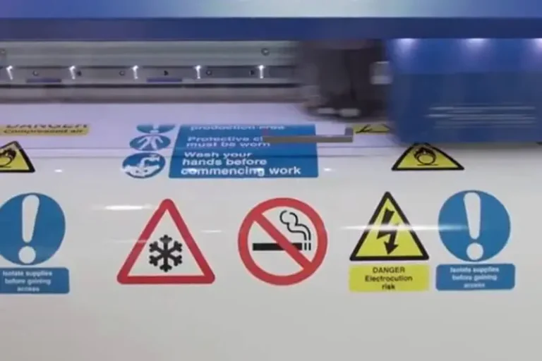 Gros plan des panneaux d'avertissement sur un traceur de découpe, y compris les symboles de température froide, d'interdiction de fumer, de danger d'électrocution, et les instructions de porter un équipement de protection et de se laver les mains avant de commencer le travail.