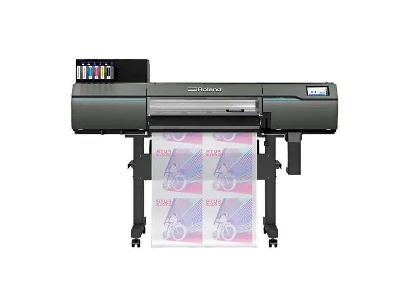 Une imprimante Roland grand format produit plusieurs feuilles d'affiches colorées avec un motif de bicyclette en utilisant la technologie d'impression DTF. Les cartouches d'encre sont visibles en haut à gauche de l'imprimante, qui repose sur quatre pieds sur un fond blanc.