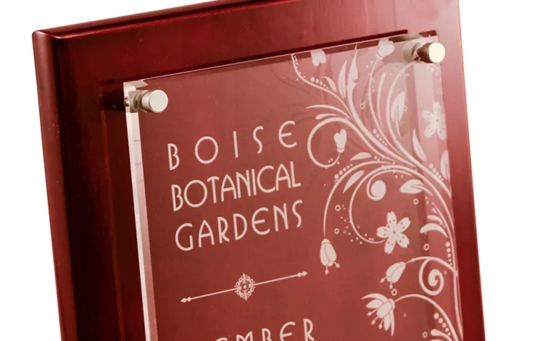 Gros plan d'une plaque avec une façade en verre, montée sur une base en bois et gravée à l'aide d'un laser graveur CO2 avec les mots Boise Botanical Gardens, joliment décorés de motifs floraux.