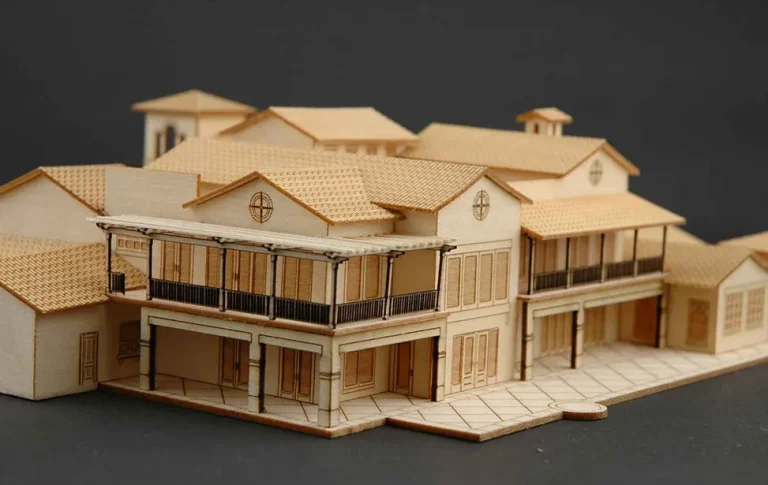 Une maquette architecturale en bois, réalisée à l'aide d'un laser découpeur, présente un bâtiment à plusieurs étages avec des balcons détaillés, des toits à pignons multiples et un trottoir, le tout sur un fond uni et sombre.