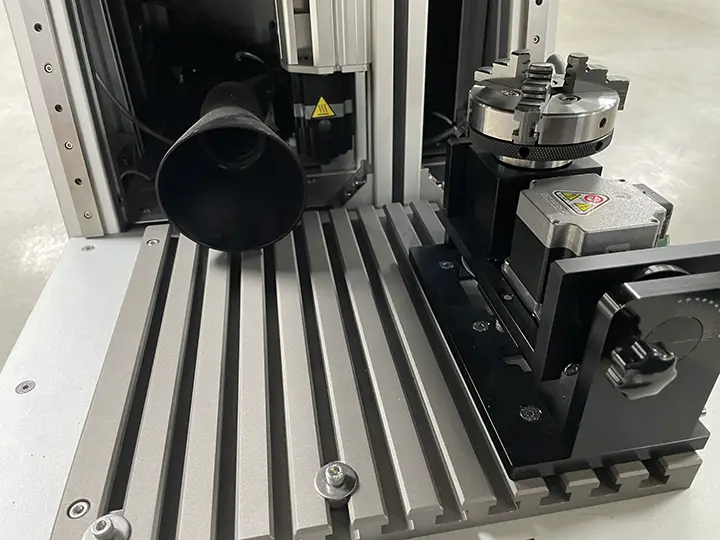 Une vue rapprochée de l'intérieur d'un laser fibre MOPA Galvo F1 avec un accessoire rotatif en option posé sur la table de travail.