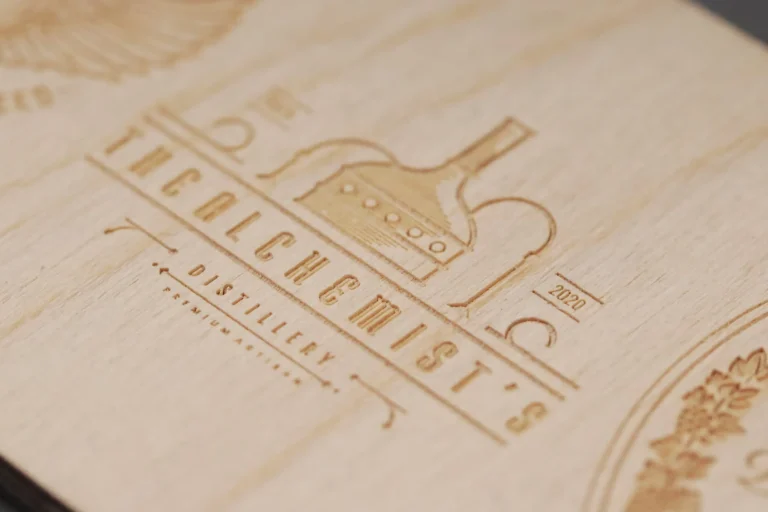 Gros plan d'une surface en bois sur laquelle est gravé un logo représentant un appareil de distillation et le texte The Alchemists Distillery 2020.