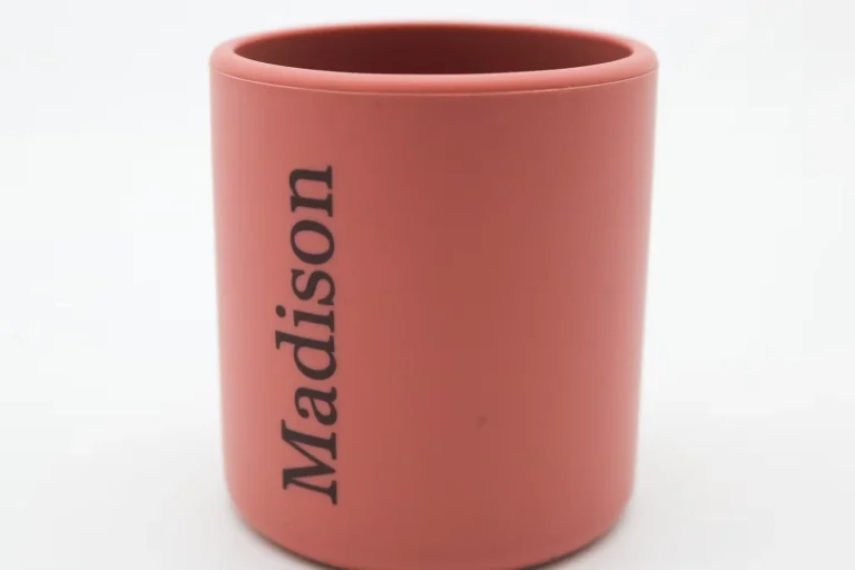 Une tasse rose mat unie, au marquage industriel, avec le mot Madison imprimé verticalement en lettres noires sur sa face, sur fond blanc.