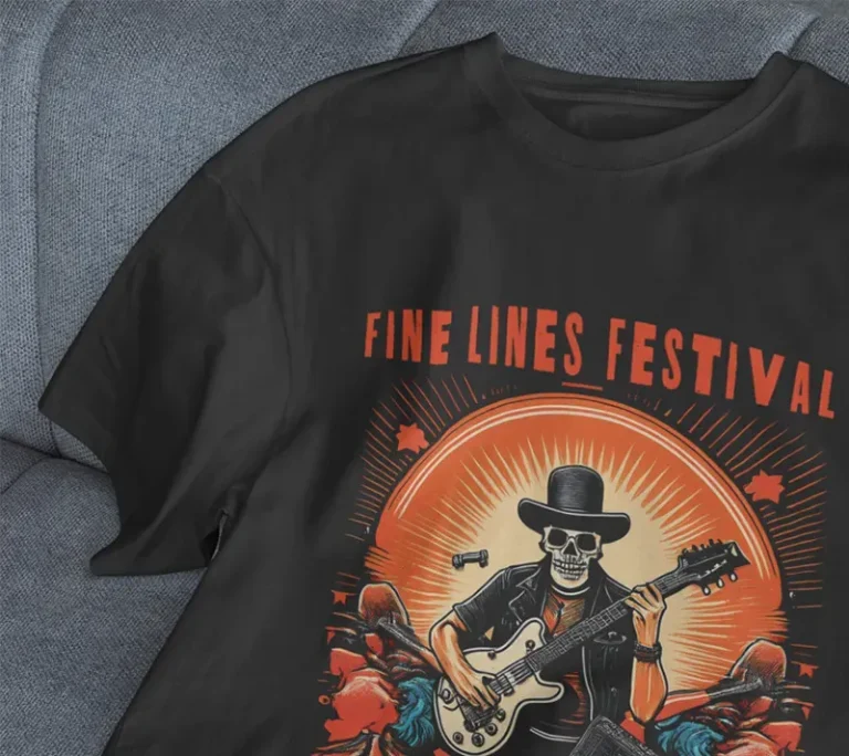 Un T-shirt noir imprimé avec l'impression DTF représente un squelette avec un chapeau et des lunettes de soleil jouant de la guitare électrique, avec FINE LINES FESTIVAL au-dessus de l'image, allongé sur un canapé gris.