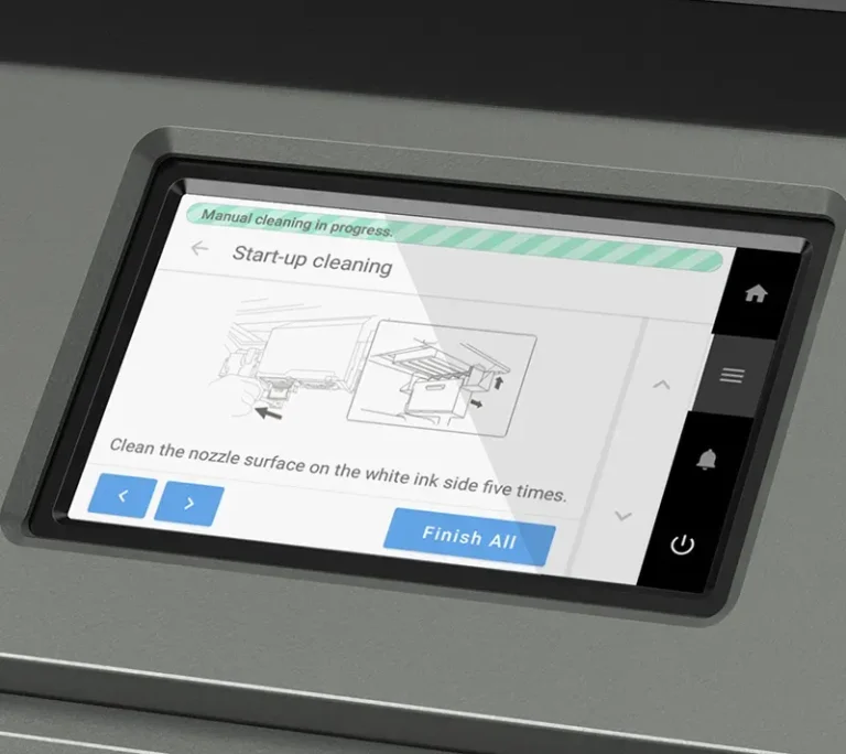 Un gros plan de l'écran tactile d'une machine d'impression DTF affiche un message de nettoyage au démarrage avec des instructions pour nettoyer cinq fois la surface de la buse du côté de l'encre blanche. Le bouton Finish All est visible en bas de l'écran.