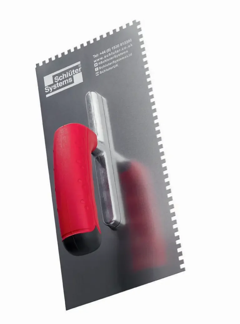 Une truelle crantée avec un manche rouge et noir et une lame métallique avec des crans sur les bords, marquée du logo Schlüter Systems et des informations de contact marquées par un laser co2 sur la surface métallique.