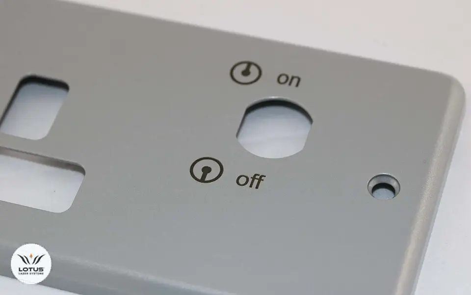 Gros plan d'un panneau métallique gris pour un marqueur laser, avec un trou circulaire étiqueté "on" en haut et "off" en bas, chacun avec des symboles de puissance. Le panneau comporte également d'autres découpes et un petit logo dans le coin inférieur gauche.