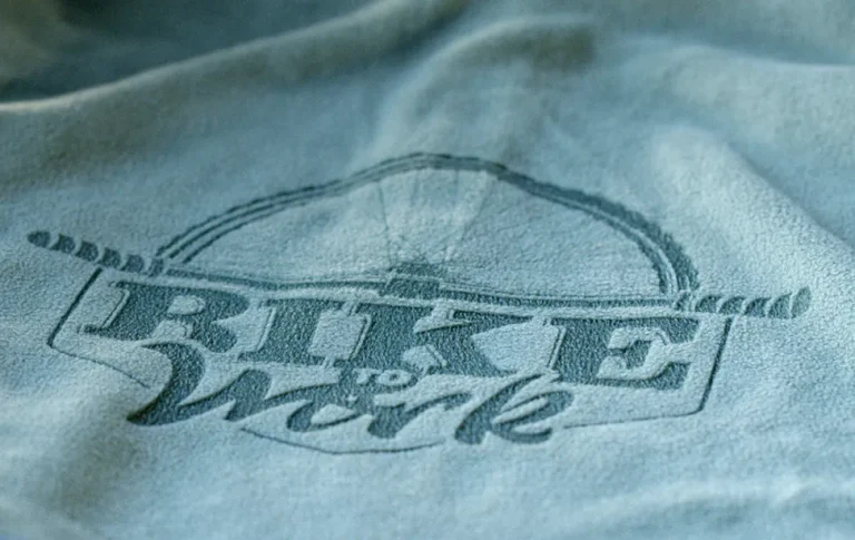 Gros plan sur un tissu bleu sur lequel la phrase Bike to Work est gravé au laser CO2 en grandes lettres, avec un graphisme subtil d'une roue de vélo au-dessus du texte.