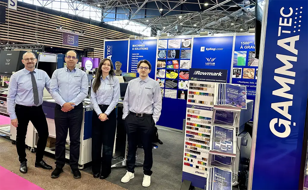 Quatre personnes portant des chemises assorties se tiennent dans un stand d'exposition au salon cprint 2026, avec des panneaux GAMMA-TEC, des présentoirs de produits, des brochures et des machines visibles à l'arrière-plan, dans une grande salle intérieure.