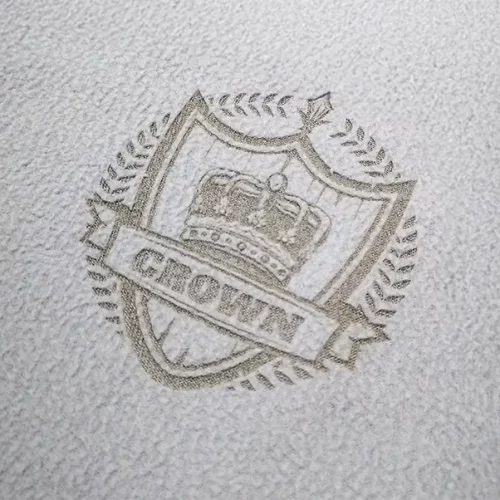 Surface texturée présentant un emblème en relief avec une couronne à l'intérieur d'un bouclier, entouré d'une couronne de laurier. Une bannière sur le bouclier affiche le mot CROWN en lettres capitales.