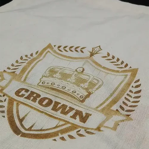 Ce sac fourre-tout en toile est orné d'un motif doré représentant une couronne au-dessus du mot CROWN à l'intérieur d'un bouclier, avec des feuilles de laurier entourant le bouclier.