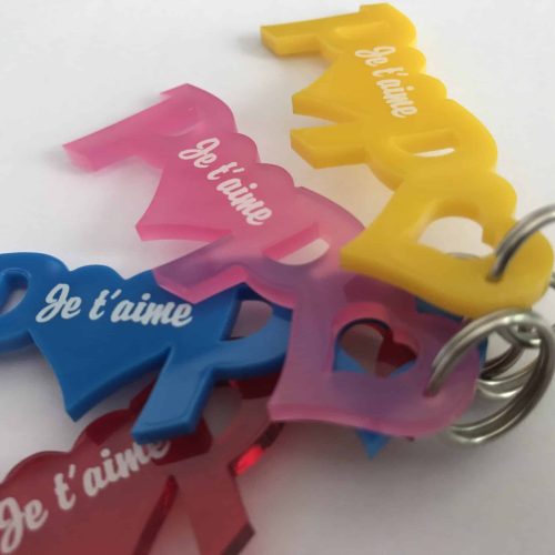 Plusieurs porte-clés en plastique coloré en forme de cœur et du mot PAPA sont empilés. Chaque porte-clés, fabriqué par un fournisseur matière à graver, comporte le mot Je t'aime en blanc et est attaché à un porte-clés en métal.