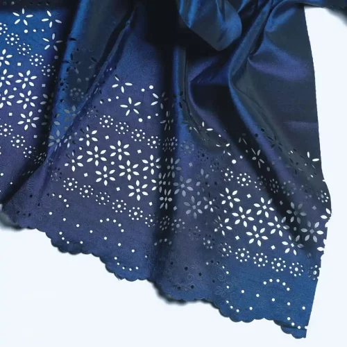 Un gros plan sur un tissu bleu foncé aux motifs floraux complexes et aux bords festonnés met en valeur une personnalisation textile exquise. Le motif présente de petites découpes délicates, créant une apparence de dentelle à la surface.