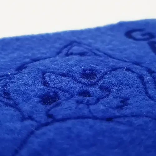 Gros plan dun tissu en feutre bleu avec le contour en relief du visage dun chat et le mot « GATO » dans le coin, mettant en valeur un textile de personnalisation exquis. La texture est luxueusement douce et duveteuse.