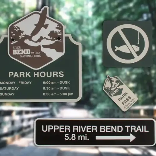 Des panneaux à lentrée dun parc indiquent les heures douverture du parc, un symbole dinterdiction de pêche, un avis de pass obligatoire pour le parc et une direction du sentier Upper River Bend, 5,8 miles. Larrière-plan présente une vue floue dun sentier boisé.