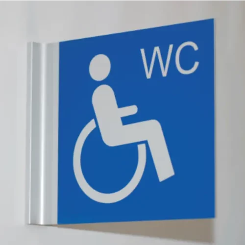 Un panneau bleu avec un symbole blanc représentant une personne en fauteuil roulant, indiquant laccessibilité aux fauteuils roulants. Les lettres « WC » sont visibles en haut à droite, indiquant des toilettes.