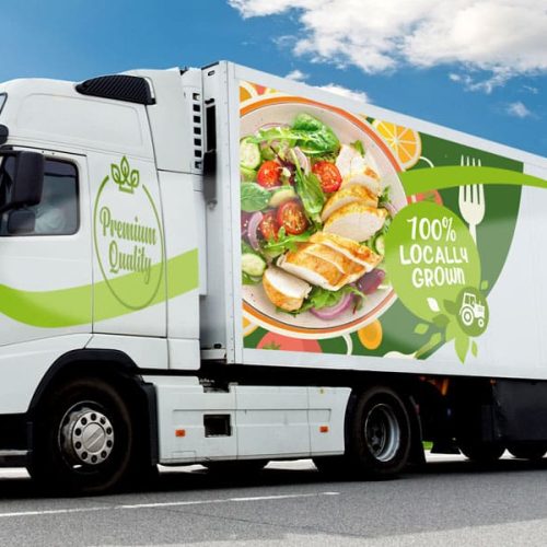 Un semi-remorque blanc au graphisme vert, créé à l'aide d'un traceur de découpe, porte les mentions "Farm food" et "100% local grown", avec une grande image d'une salade au poulet sur une route de campagne sous un ciel bleu.