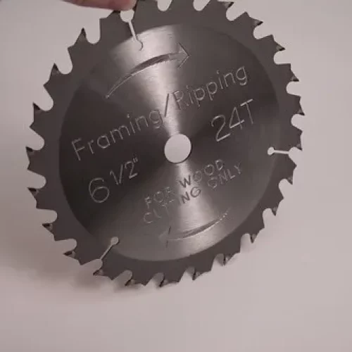 Une lame de scie circulaire marquée "Framing/Ripping 6 1/2 24T For Wood Cutting Only" est représentée debout sur une surface blanche, avec une main tenant son bord supérieur - idéale pour les projets en bois et compatible avec diverses machines de fraisage d'héliogravure.