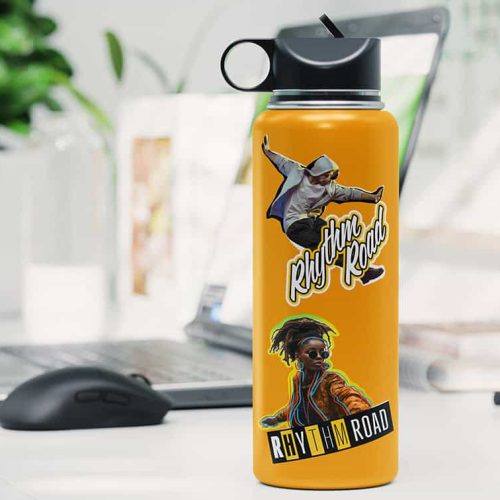 Une bouteille deau jaune est posée sur un bureau décoré dautocollants de danseurs et du texte « Rhythm Road », à côté dune imprimante/découpeuse à jet dencre. Larrière-plan révèle un décor de bureau avec une plante et un écran dordinateur flou, ajoutant une touche de créativité vibrante à lespace de travail.
