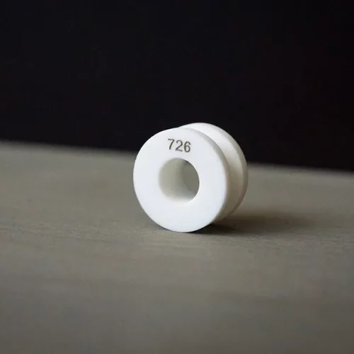 Un petit objet cylindrique blanc avec un trou central et le nombre 726 imprimé dessus, probablement marqué à l'aide d'un marqueur laser co2, placé sur une surface plane sur un fond sombre.