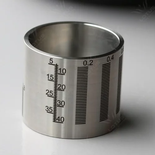 Un gobelet gradué cylindrique en acier inoxydable avec des marques noires précises, créées par marqueur laser, en millilitres et en onces sur son côté, placé sur une surface blanche.
