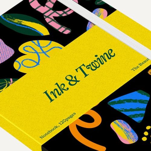 Un carnet avec une bande jaune étiquetée Ink & Twine est fermé. La couverture noire présente des formes abstraites colorées, maintenues par des élastiques blancs - une impression d'objet élégante. La mention "Carnet de notes, 120 pages" est imprimée sur le dos.