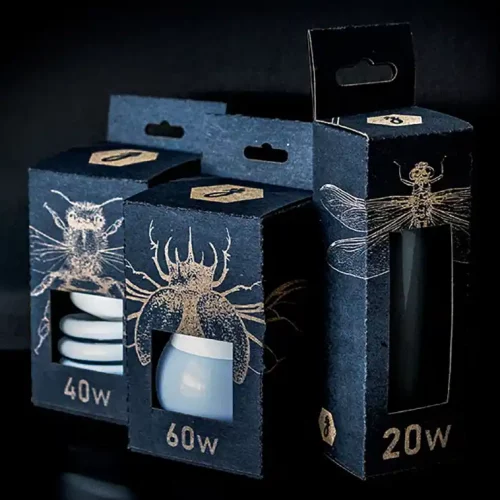 Trois boîtes en carton bleu foncé avec des illustrations dinsectes découpées et gravées sur papier, chacune abritant une ampoule étiquetée avec différentes puissances : 40 W, 60 W et 20 W. Les boîtes présentent un design moderne et sont astucieusement disposées sur un fond noir.