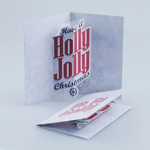 Une carte de vœux pliée sur fond blanc affiche le message « Have a Holly Jolly Christmas » en lettres rouges et noires. Dotée dune découpe et dune gravure sur papier, la carte est légèrement ouverte, révélant une carte finement conçue en dessous.