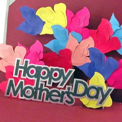 Une carte pop-up comportant des fleurs en papier colorées en rose, bleu, jaune et rouge présente magnifiquement la découpe et la gravure du papier autour dun message « Bonne fête des mères » sur un fond rouge vif.