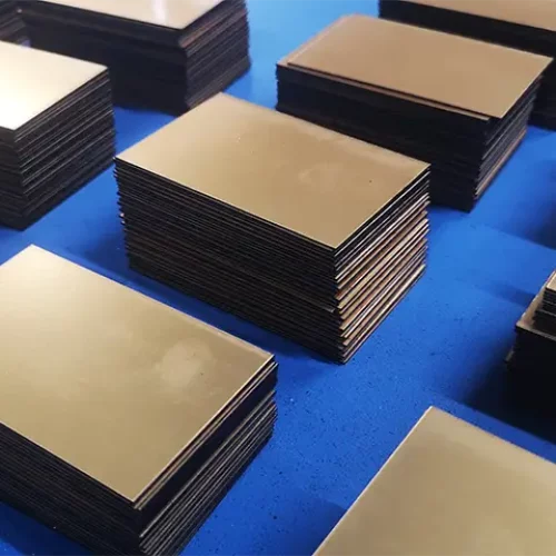 Des piles de plaques de laiton vierges et rectangulaires sont disposées en rangées sur une surface bleue. La finition métallique réfléchissante brille comme si elle avait été préparée pour une découpe précise à l'aide d'une scie circulaire Varga, et les plaques sont empilées uniformément en plusieurs piles.